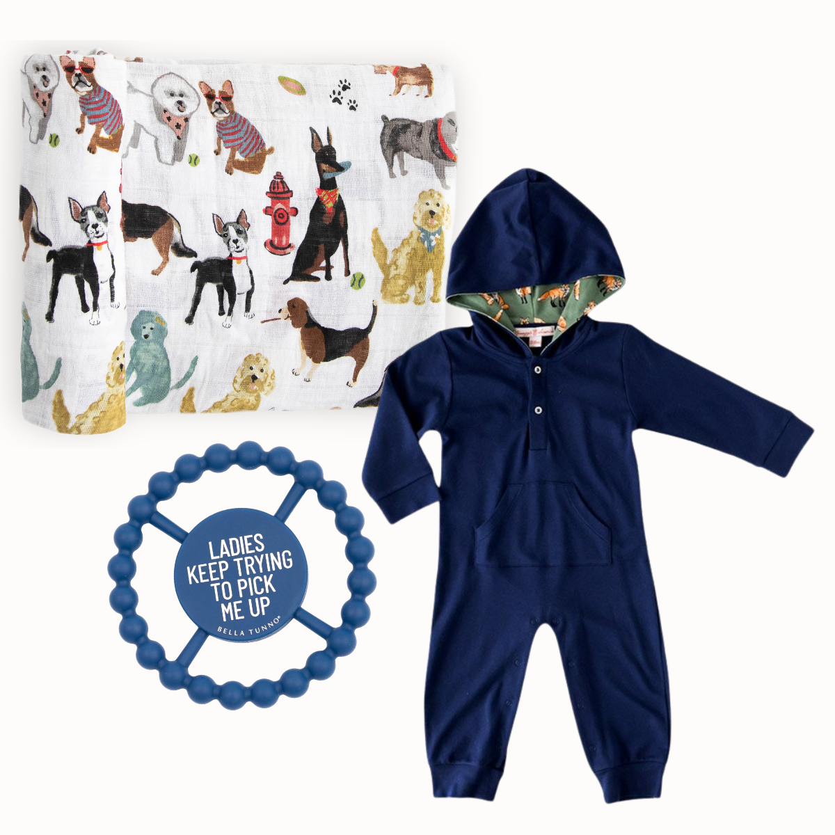 A baby gift set featuring a navy blue hooded romper, a white muslin blanket with a colorful dog pattern, and a blue beaded teething ring with a printed quote. Little Birdies Puppy Love Gift Set for baby boy