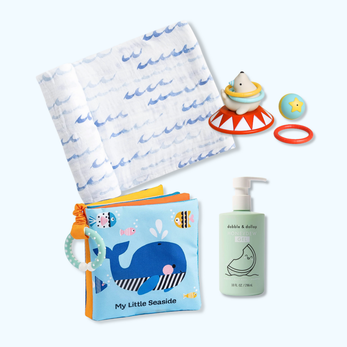 A baby gift set featuring a blue and white whale-themed baby book, a white muslin cloth with blue wave prints, a bubble & baby baby bottle, a shark toy, and a star ball on a light blue background. Little Birdies Splish Splash Gift Set Bath Time