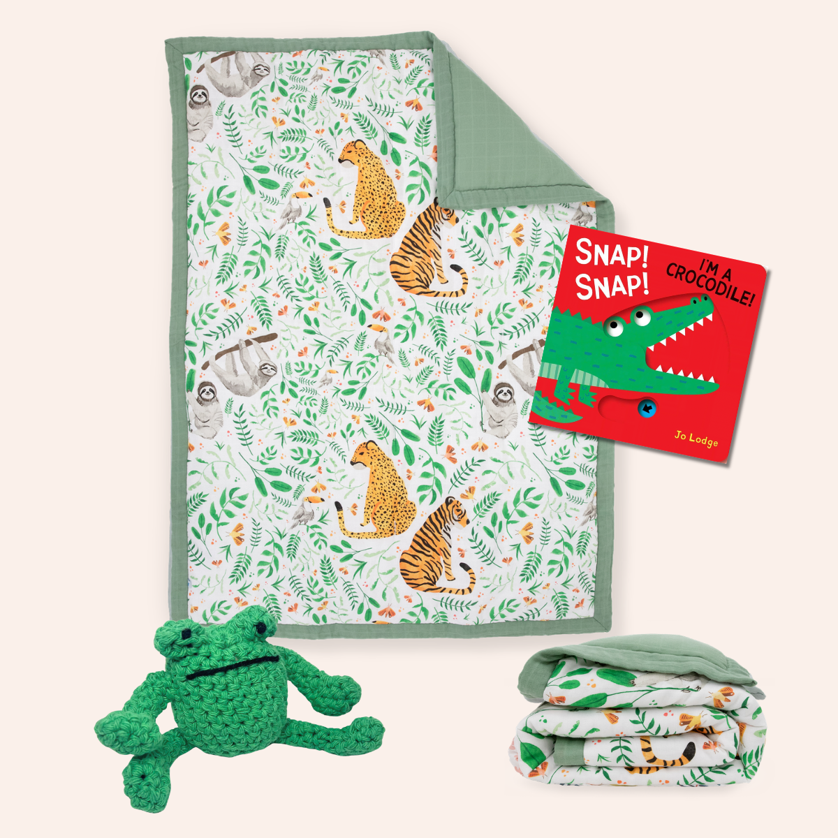A baby gift set featuring a jungle-themed quilted blanket with animal prints, a green crocodile plush toy, a folded matching blanket, and a children's book titled 'Snap! Snap! I'm a Crocodile!' by Dr. Ludwig, arranged on a light beige background.